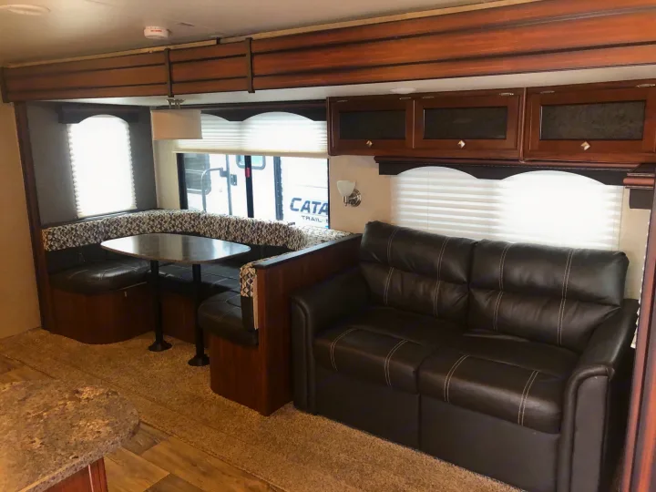 Comfortable RV rental interior featuring a spacious dinette booth, a plush sofa, and overhead cabinets for storage.. Heartland M29 2017