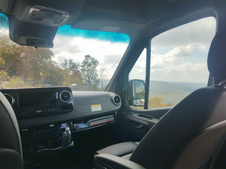 Inside an RV rental, a sleek dashboard and passenger seat offer a stunning view of mountainous landscapes and cloudy skies.. Winnebago Revel 2020