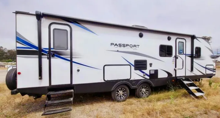 A white Passport travel trailer RV with blue and black graphics, two doors, and steps. Perfect for an RV rental.. Keystone RV Passport GT 2021