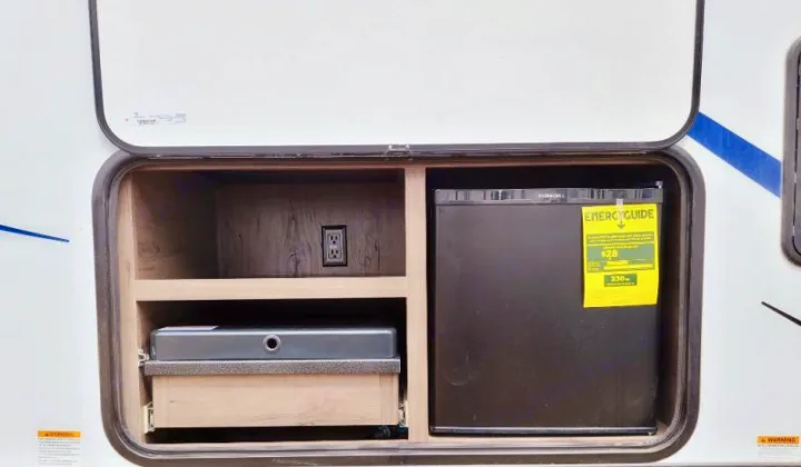This rv rental features an outdoor kitchen with a compact fridge, cooktop, and electrical outlet in a side compartment.. Keystone RV Passport GT 2021