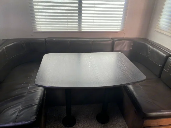 U-shaped leatherette dinette booth with a dark wood table in an RV rental, ideal for dining or lounging.. Keystone RV Passport GT 2021