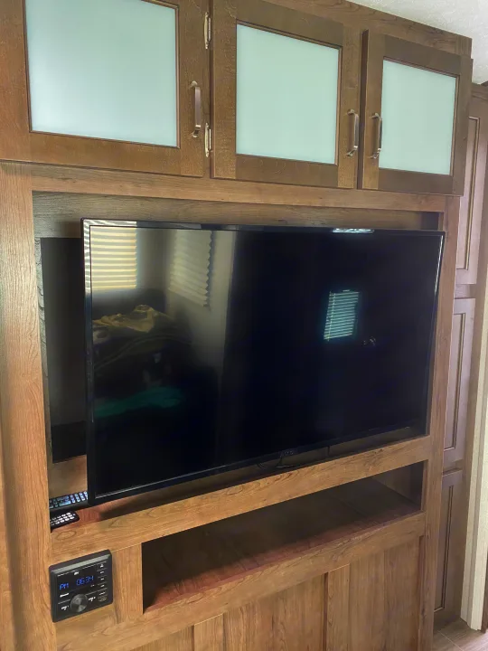 RV rental interior: Detailed view of a wood entertainment center with frosted glass cabinets, TV, and an RV media console.. Keystone RV Passport GT 2021