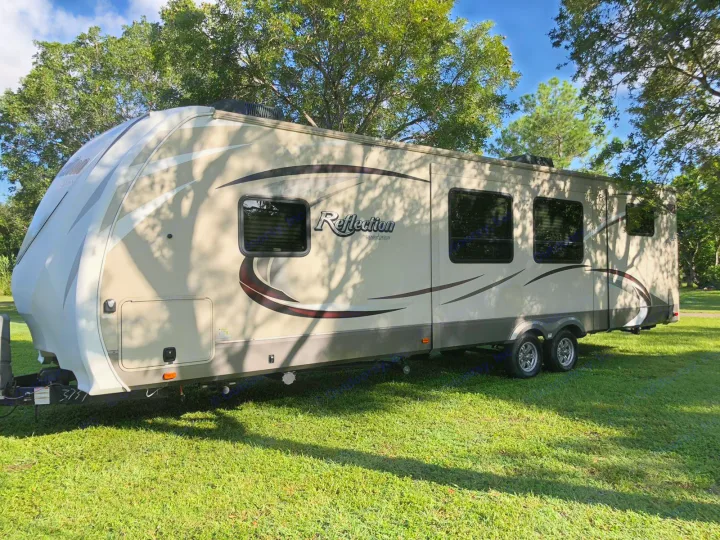 A sleek, light-colored Reflection Grand Design RV rental travel trailer sits on lush green grass, perfect for camping.. Grand Design Reflection 2016
