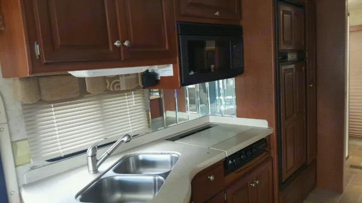 Explore this RV rental's functional kitchen: wood cabinets, dual sink, microwave, stovetop, and built-in fridge.. THOR Four Winds Infinity 2005