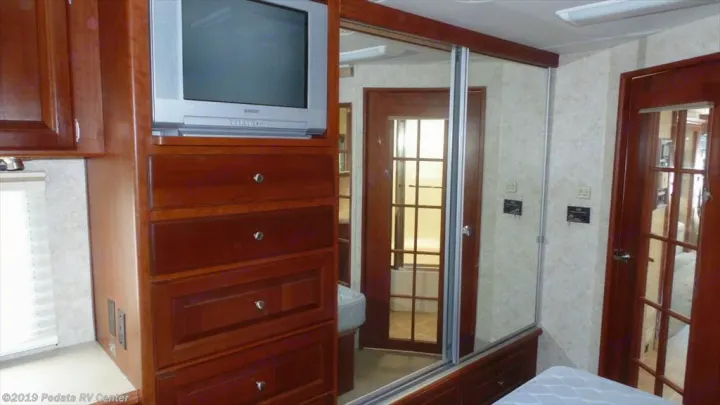 RV rental bedroom with TV, wood drawers, and mirrored closet reflecting the bathroom area.. THOR Four Winds Infinity 2005