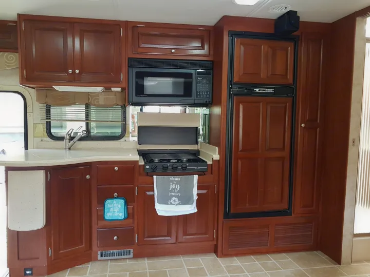 Well-equipped rv rental kitchen featuring warm wooden cabinetry, a modern sink, microwave, 3-burner stove, and a fridge unit.. THOR Four Winds Infinity 2005