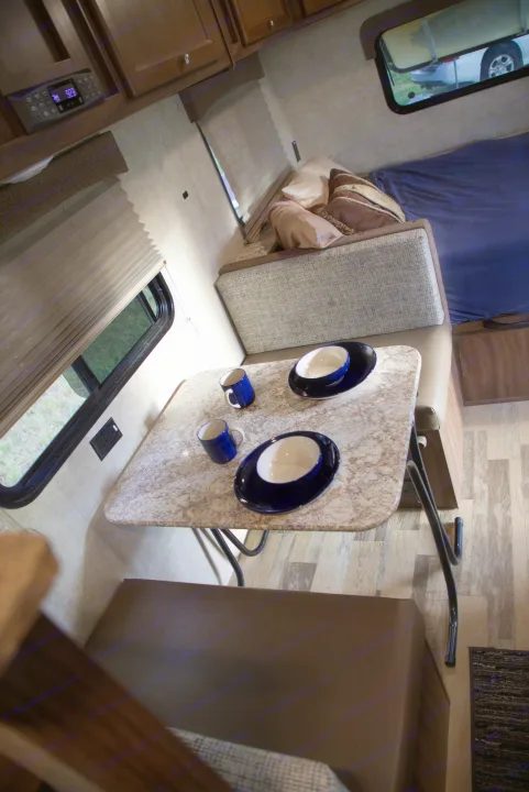 Inside an RV rental: a neat dining table with blue dishware, bench seats, and a sleeping area, showcasing comfortable living.. Forest River Other 2018