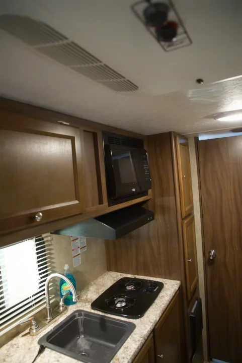 RV rental kitchen: Features a microwave, gas stovetop, sink, and wood cabinets. The bright window illuminates the area.. Forest River Other 2018