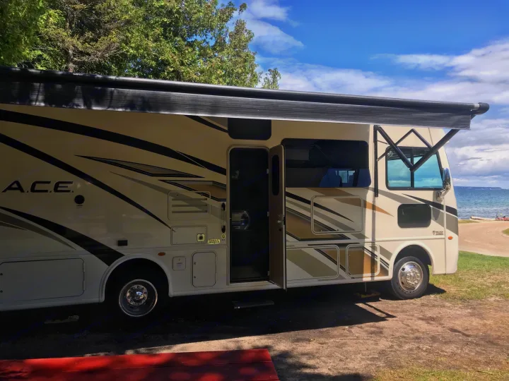 Spacious RV rental with extended awning by a clear lake under blue skies. Perfect for an outdoor camping vacation.. Other A.C.E 2020