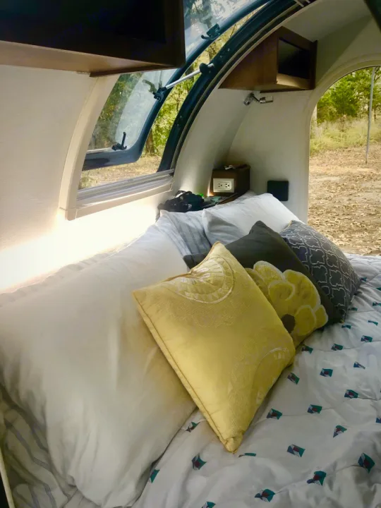 Enjoy a cozy night's sleep in this RV rental! Interior view of a comfortable bed with colorful pillows and an open window.. Nucamp T@G MAX 2018