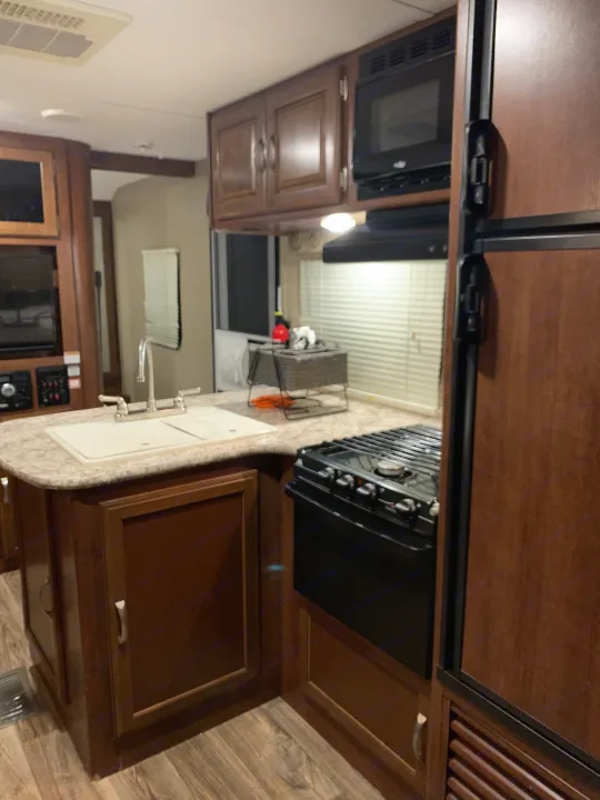 Compact RV rental kitchen with sink, stove, microwave, and wood cabinets, offering efficient space utilization.. Keystone RV Passport Elite 2017