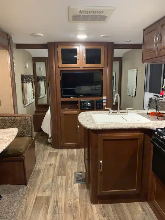 Spacious RV rental interior featuring a kitchen with sink, dinette booth, entertainment center, and wood cabinets.. Keystone RV Passport Elite 2017