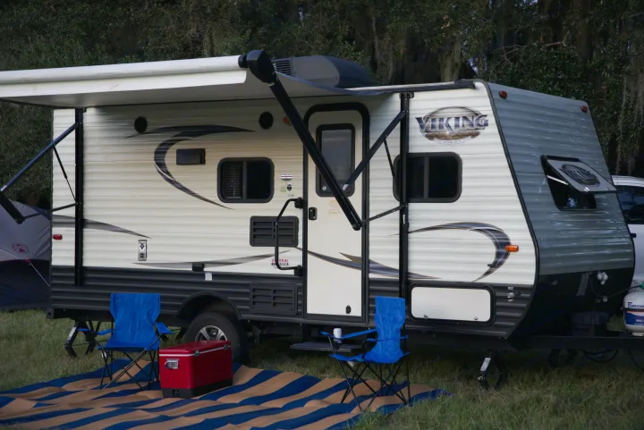 RV rental travel trailer with an extended awning, blue chairs, and a red cooler on a striped mat for outdoor camping.. Forest River Other 2018