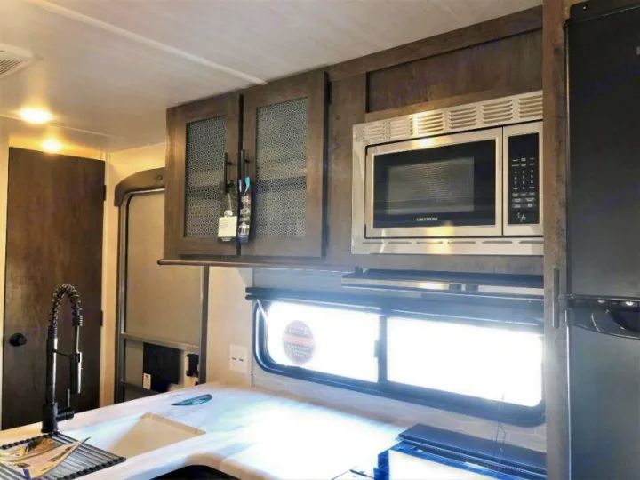 Inside this RV rental, find a compact kitchen with a sink, stainless microwave, and patterned cabinets.. Forest River Salem 2021