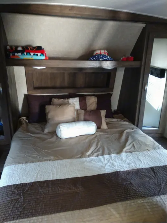 Cozy RV rental bedroom with striped bedding, pillows, and compact storage in wooden cabinets.. Forest River Vibe 2018