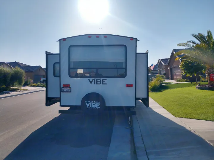 A white Vibe travel trailer, possibly an rv rental, with slide-outs extended, parked on a sunny residential street.. Forest River Vibe 2018