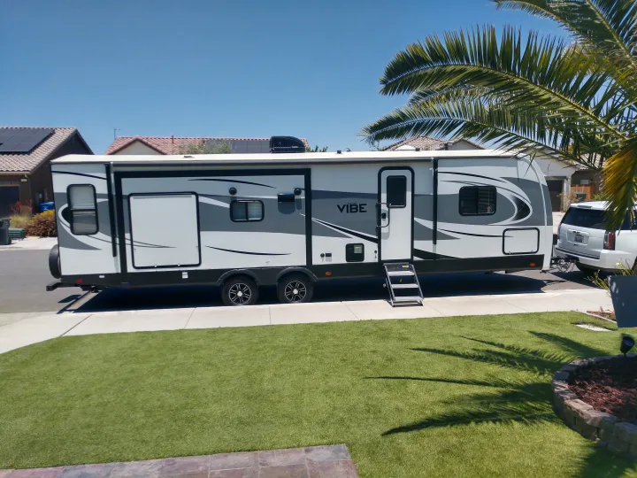A large white Vibe RV rental is parked on a sunny residential street with houses and palm trees.. Forest River Vibe 2018