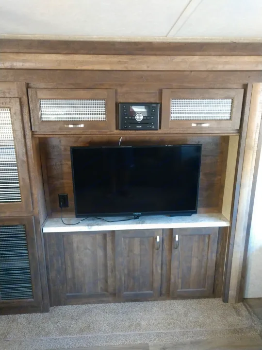 Modern RV rental entertainment center with flat-screen TV, stereo, and wood storage cabinets.. Forest River Vibe 2018