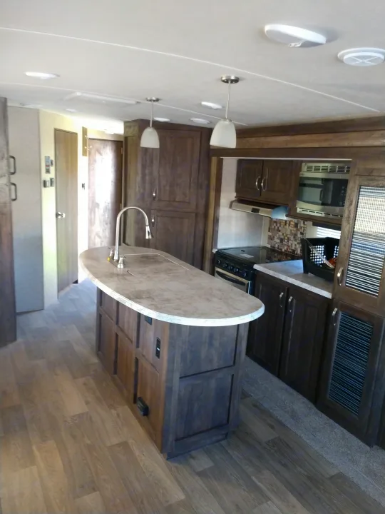 Experience this RV rental's modern interior. A well-equipped kitchen with dark wood cabinets, appliances, an island, and wood-look flooring.. Forest River Vibe 2018