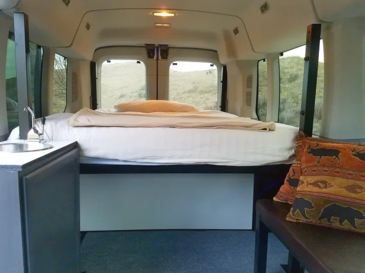 Cozy rv rental interior: comfortable bed, functional sink, and scenic outdoor views from the windows.. Ford transit 2019