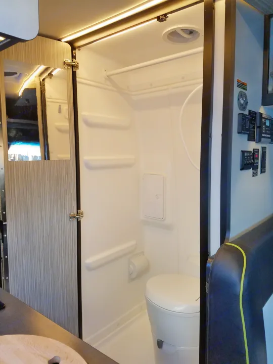 Compact RV rental wet bath interior featuring a toilet, shower, mirror, LED lighting, and essential controls.. Winnebago Revel 2020