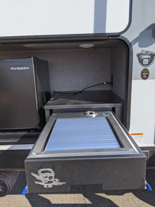 An RV rental's side compartment reveals a pull-out outdoor kitchen with a grill and RVISION mini-fridge for camping.. Jayco White Hawk 2021