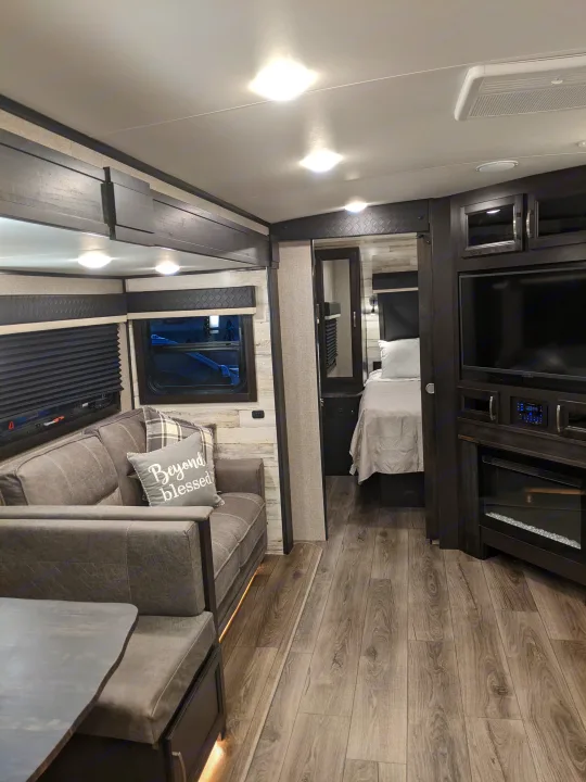 Spacious RV rental interior featuring a comfortable living area with TV & fireplace, plus a cozy bedroom beyond.. Jayco White Hawk 2021