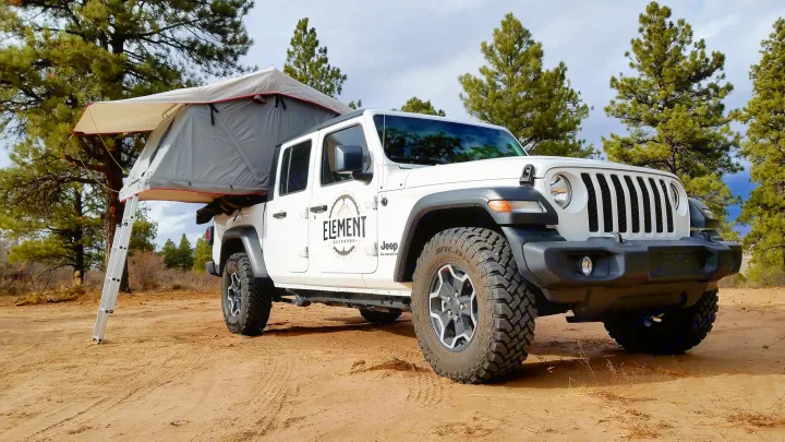 A white Jeep Gladiator truck with a deployed rooftop tent and ladder, available for rv rental for outdoor adventures.. Jeep Gladiator 2020