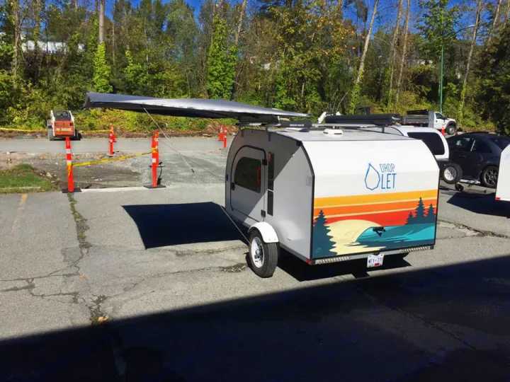 A compact teardrop camper, available for rv rental, displays a colorful graphic and an extended awning in a paved lot.. DROPLET 58 2019