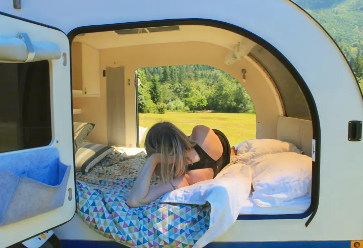 Woman relaxes in an RV rental, enjoying the scenic view from her cozy bed.. DROPLET 58 2019