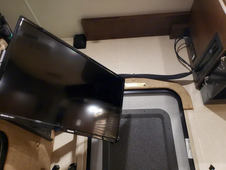 RV rental interior shows a mounted Philips TV, organized cables, and overhead shelf near a screened door.. Coachmen Other 2018