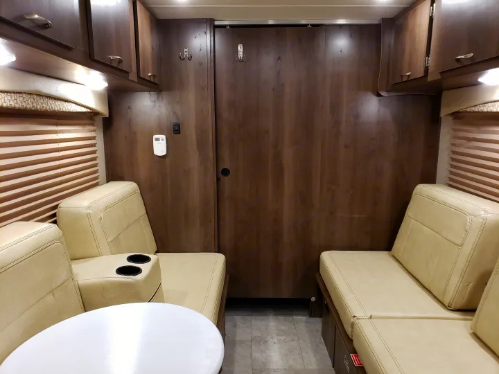 RV rental interior: beige cushioned seating with a table, dark wood cabinets, and blinds. A compact, functional living space for travel.. Coachmen Other 2018