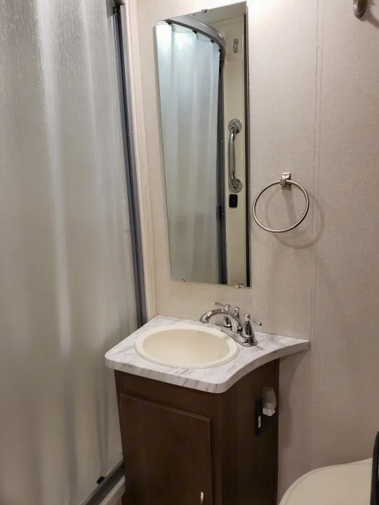 This compact RV rental bathroom features a corner sink, mirror, shower, and grab bar, with a towel ring on the wall.. Coachmen Other 2018