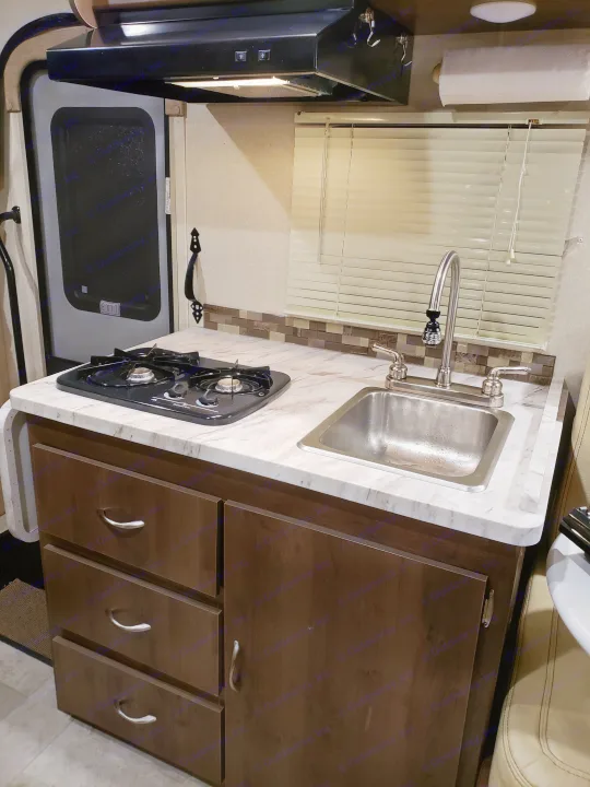 This RV rental kitchen features a compact two-burner stove, stainless steel sink, wood cabinets, and overhead lighting for travel.. Coachmen Other 2018