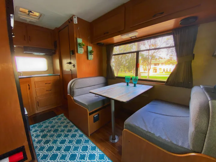 Cozy RV rental interior with a dinette, kitchen area, and a large window view, highlighted by a teal patterned rug.. Thor Motor Coach Four Winds Majestic 2017