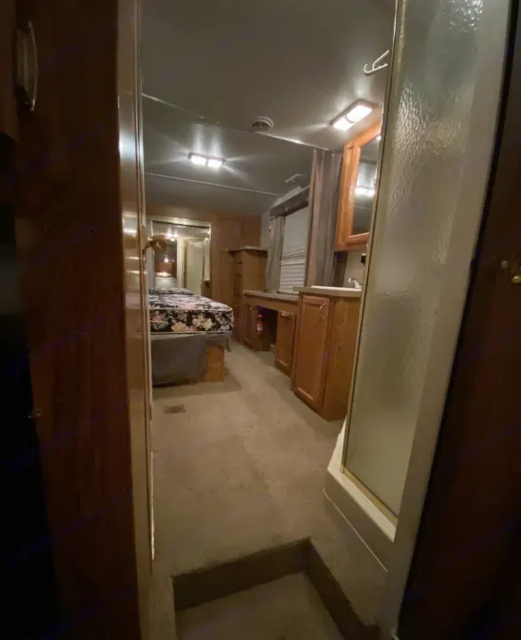 This cozy RV rental interior features a carpeted hallway leading to a bedroom with a bed and a bathroom with a shower.. Forest River Other 2012