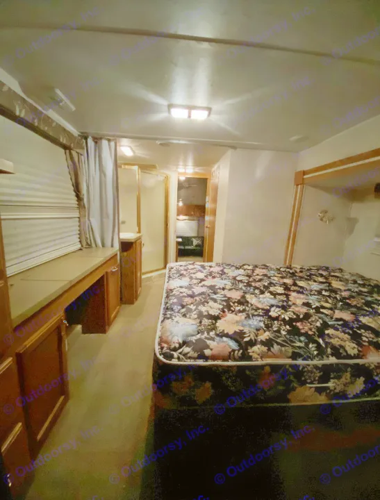 An RV rental's compact interior: a dark floral bed, a built-in desk area, and a glimpse of the bathroom beyond.. Forest River Other 2012