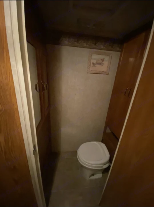 Compact RV rental bathroom with white toilet, framed art, and wood cabinetry.. Forest River Other 2012
