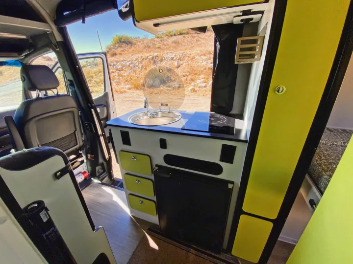 Inside a modern rv rental camper van: kitchen with sink, stove, fridge, and bright green accents. View of dry landscape.. Winnebago Revel 2020