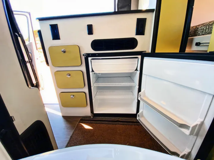 View inside an RV rental, featuring an open compact refrigerator/freezer, storage drawers, and power outlets.. Winnebago Revel 2020
