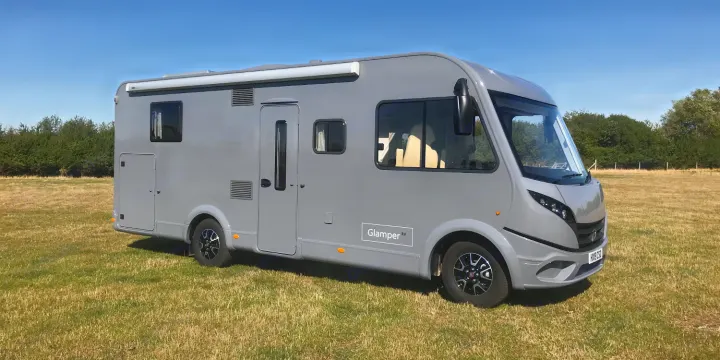 A sleek gray motorhome, an ideal RV rental, sits on a sunny grass field under a clear blue sky, perfect for travel.. GlamperRV DBL 2026