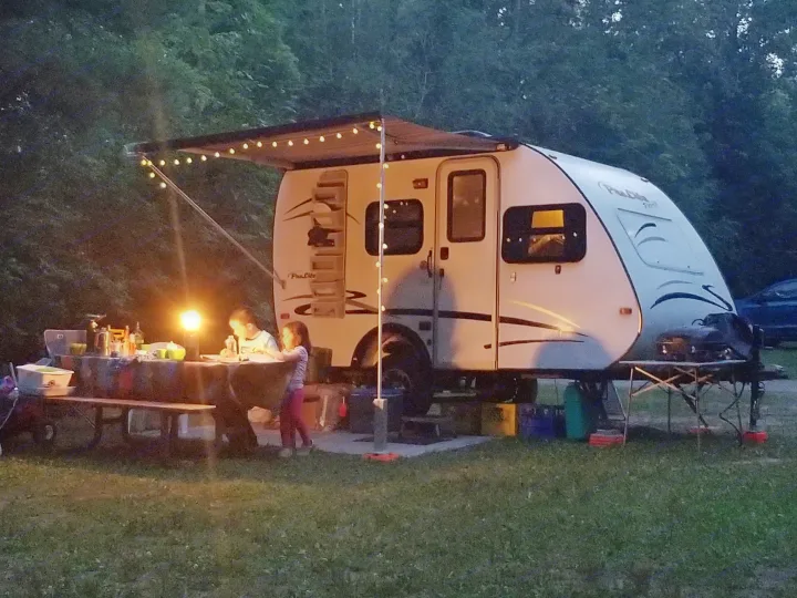 Two kids enjoy a lighted outdoor meal by their RV rental at a cozy campsite, perfect for evening adventures under string lights.. Prolite Prolite Trailer 2015
