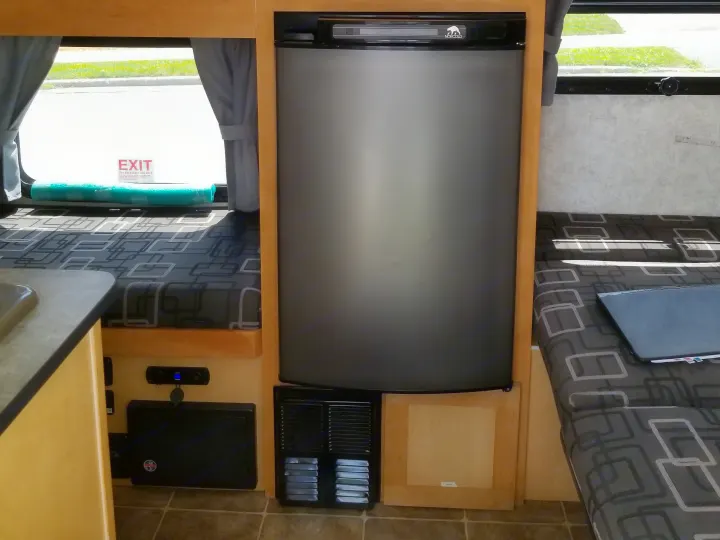 RV rental interior: Norcold refrigerator, patterned seating, and an emergency exit window with blue foam padding.. Prolite Prolite Trailer 2015