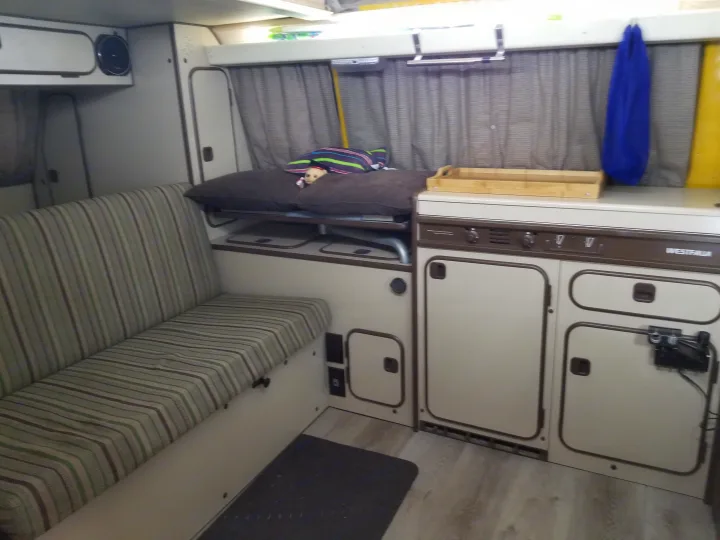 Interior of an RV rental: a cozy camper van with striped sofa, bed, kitchen, and storage, ready for adventure.. Volkswagen Westfalia 1982