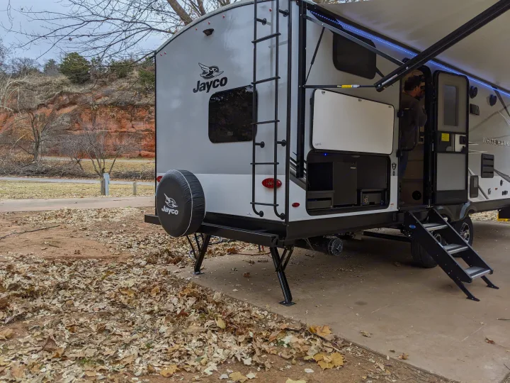RV rental: Jayco travel trailer at a fall campsite by red cliffs. Features include outdoor kitchen & open door with person inside.. Jayco White Hawk 2021