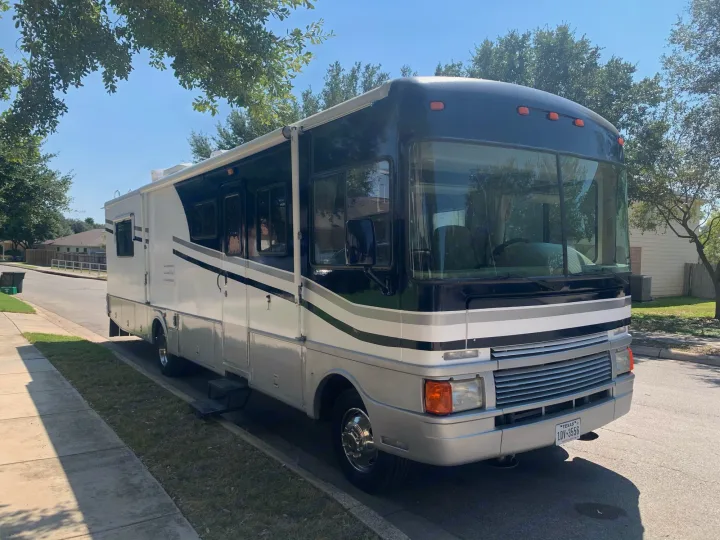 This large black, white, and grey RV rental is parked on a sunny residential street, ready for your next road trip adventure.. Fleetwood Bounder 1999