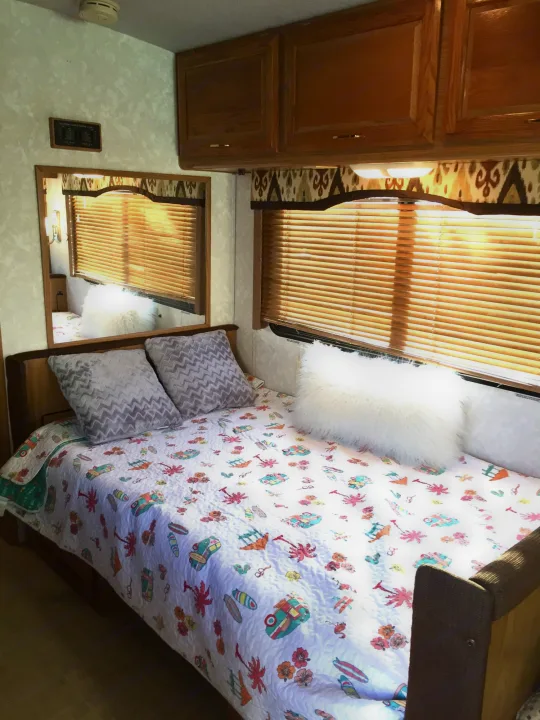 RV rental's inviting bedroom: colorful bedding, comfy pillows, window with blinds, and wood storage. Perfect for travel.. Fleetwood Bounder 1999
