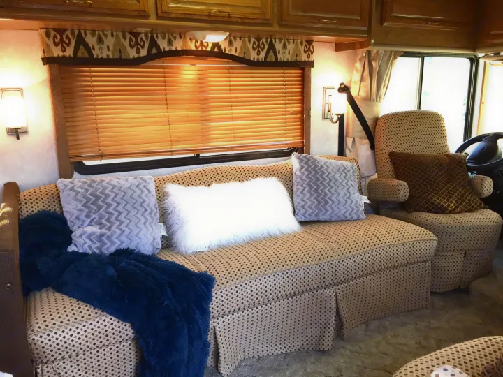 Relax in this cozy RV rental living space, featuring a patterned sofa, armchair, plush pillows, and a soft blue blanket.. Fleetwood Bounder 1999