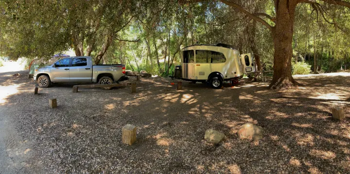 Shaded campsite scene with a silver pickup truck and an Airstream travel trailer, ideal for your next rv rental.. Airstream Basecamp 2023
