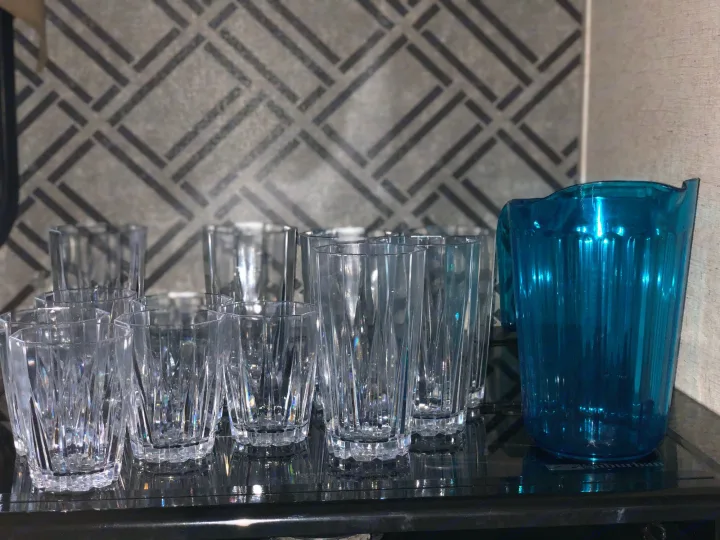 Inside an RV rental, clear glasses and a blue pitcher are neatly arranged on a dark, reflective surface.. Heartland M29 2017